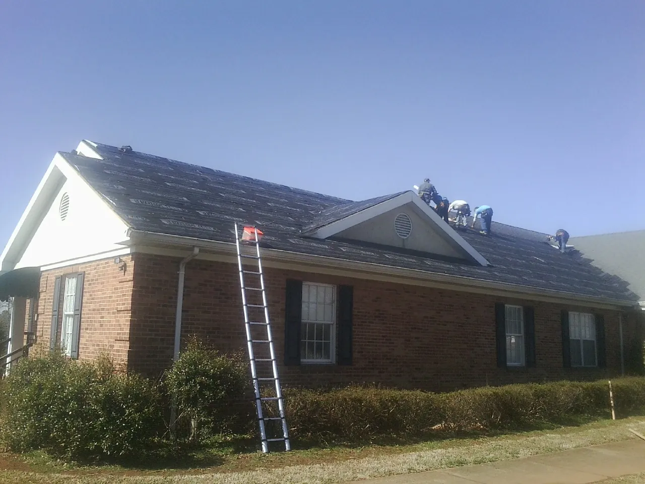 Crew tearing shingles off a brick ranch roof with a ladder set — Metal Roof Repair work by our crew in Rebersburg