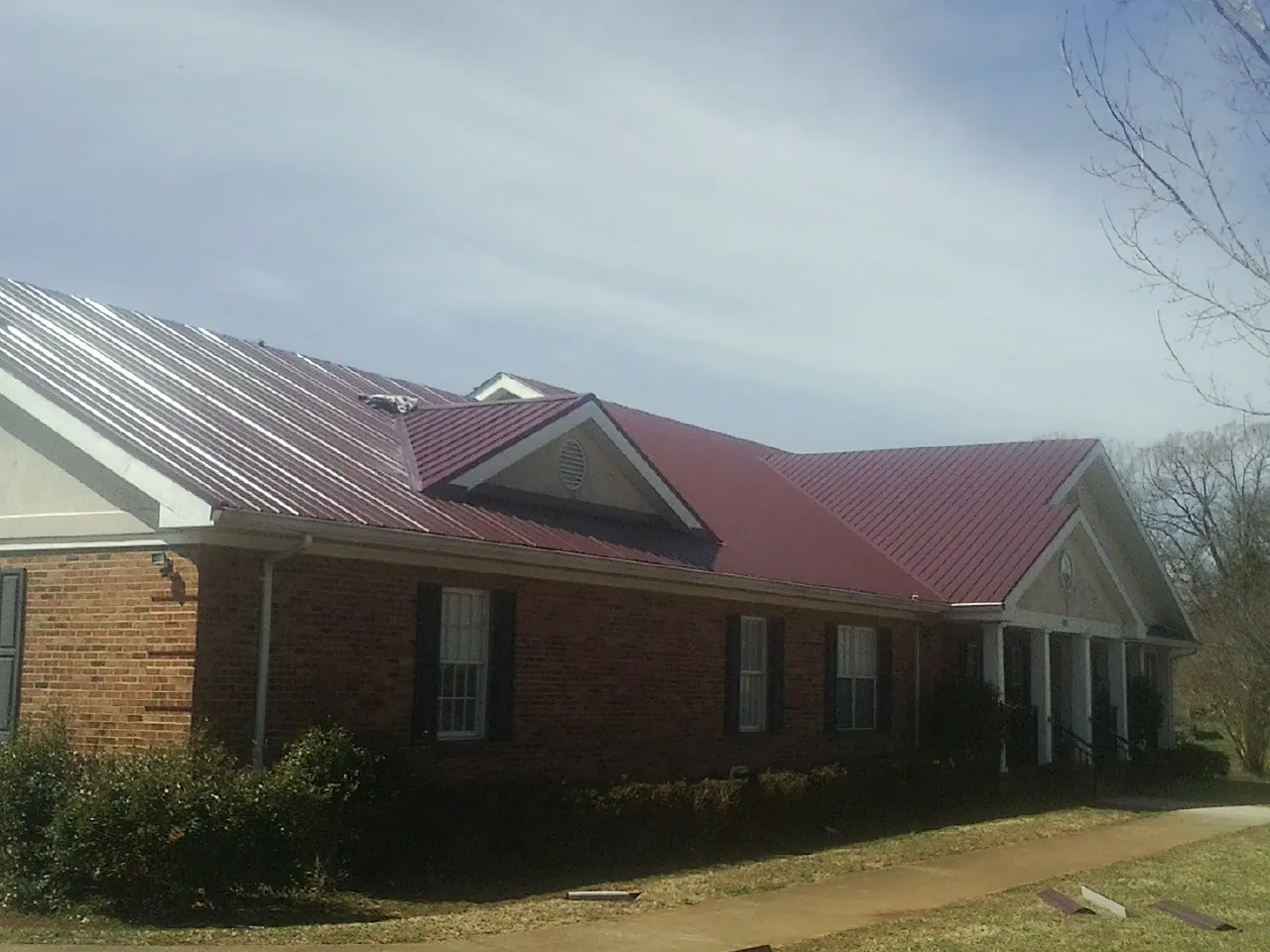 Red metal roof with gabled entries on a long brick building, from a Hail Damage Roof Repair job in Rebersburg