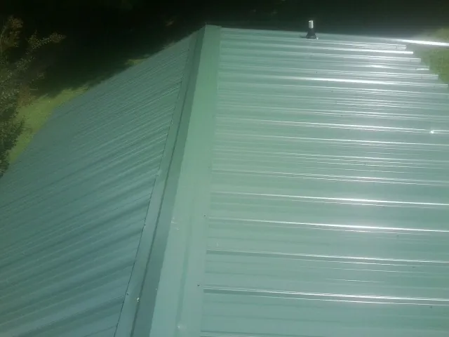 New green metal panels meeting at the ridge of a roof — Flat Roof Repair work by our crew in Rebersburg