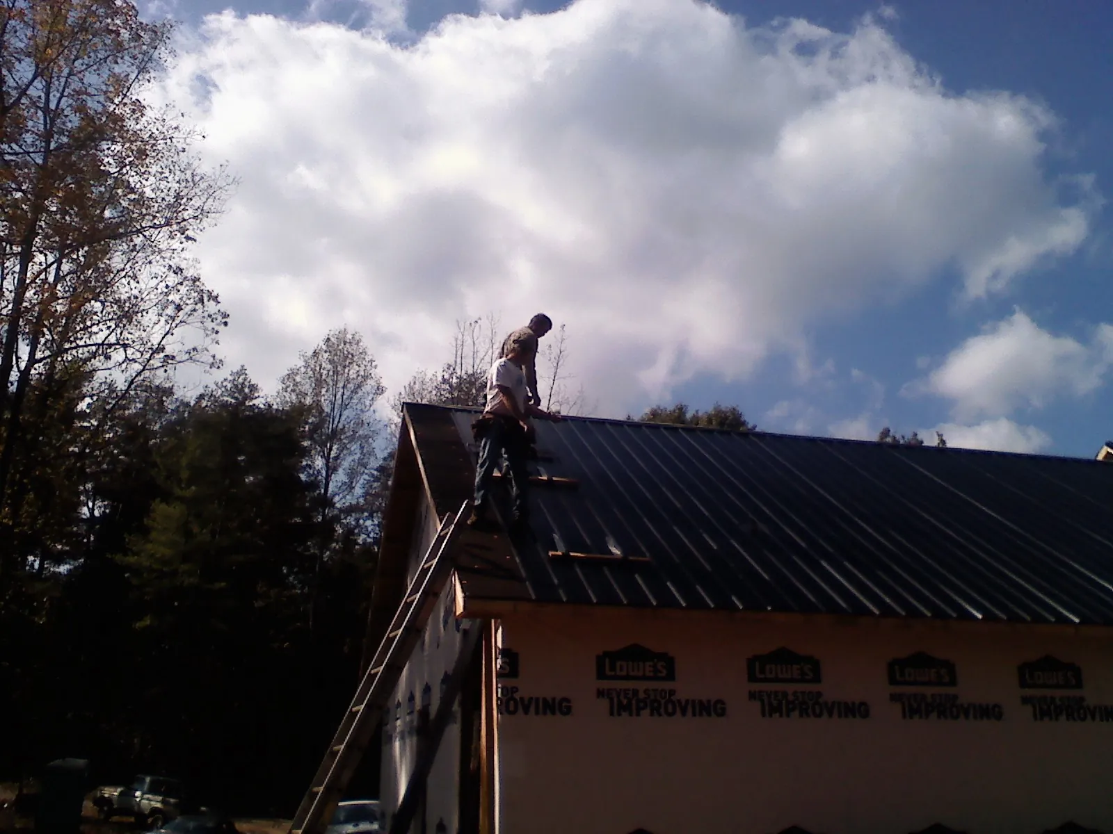 Roofer fastening dark metal panels high against a cloudy sky, from a Roof Inspection job in Rebersburg