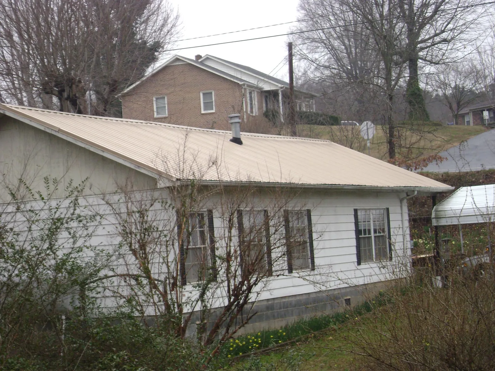 Tan metal roof on a white sided house set into a hillside — Commercial Roofing by Roofing Brothers in Rebersburg